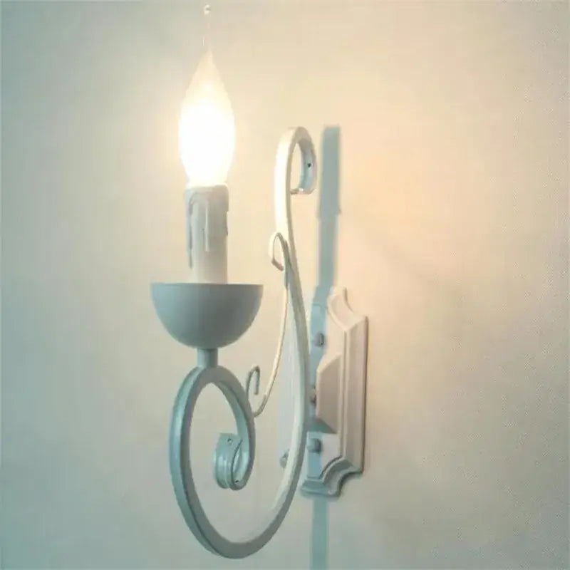 A delicate light blue elegant white iron wall lamp with ornate scrollwork and a single candle-style bulb by decorbites