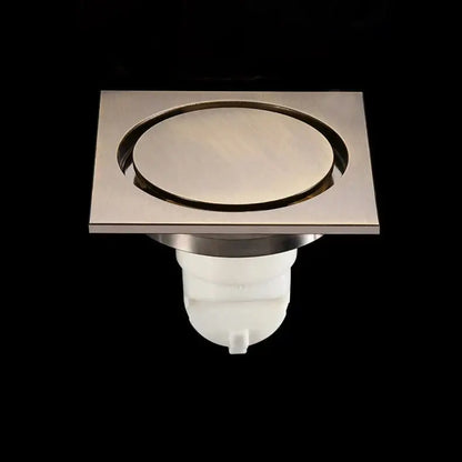 Embossed floral black brass square floor drain with brushed stainless steel circular center and white plastic base for shower room