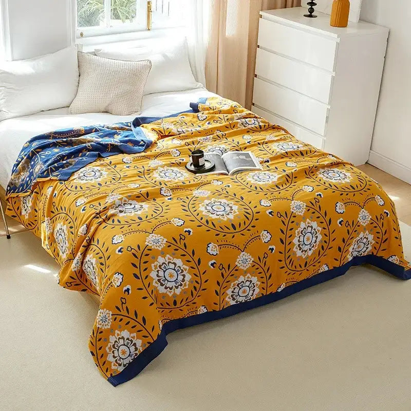 Vibrant yellow throw blanket with intricate white and navy floral patterns and navy border made of decorbites cotton gauze
