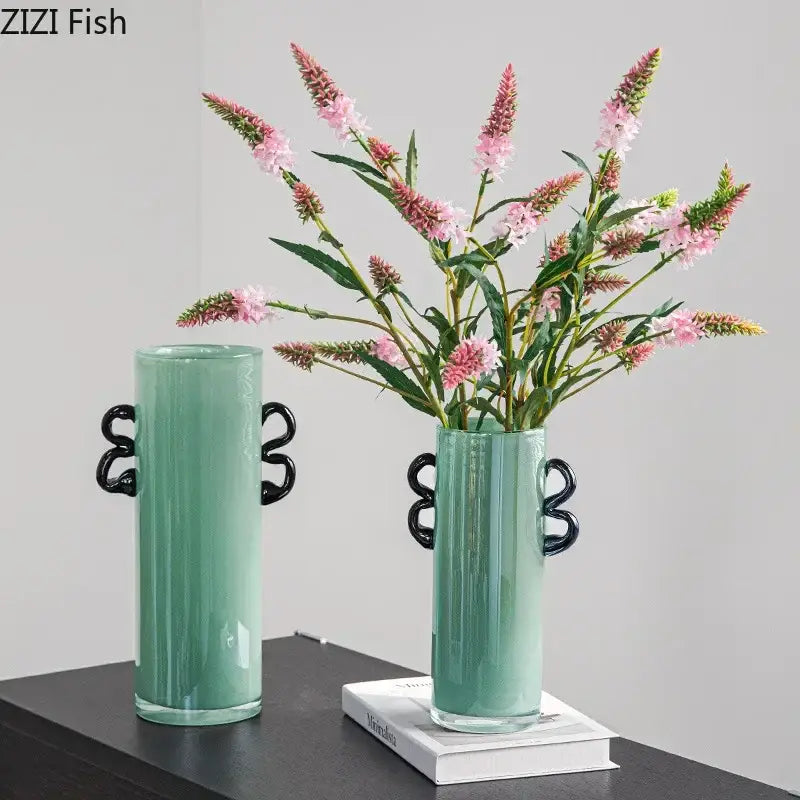 Emerald green glass vase with black s-shaped handles holding pink flowers for living room decor