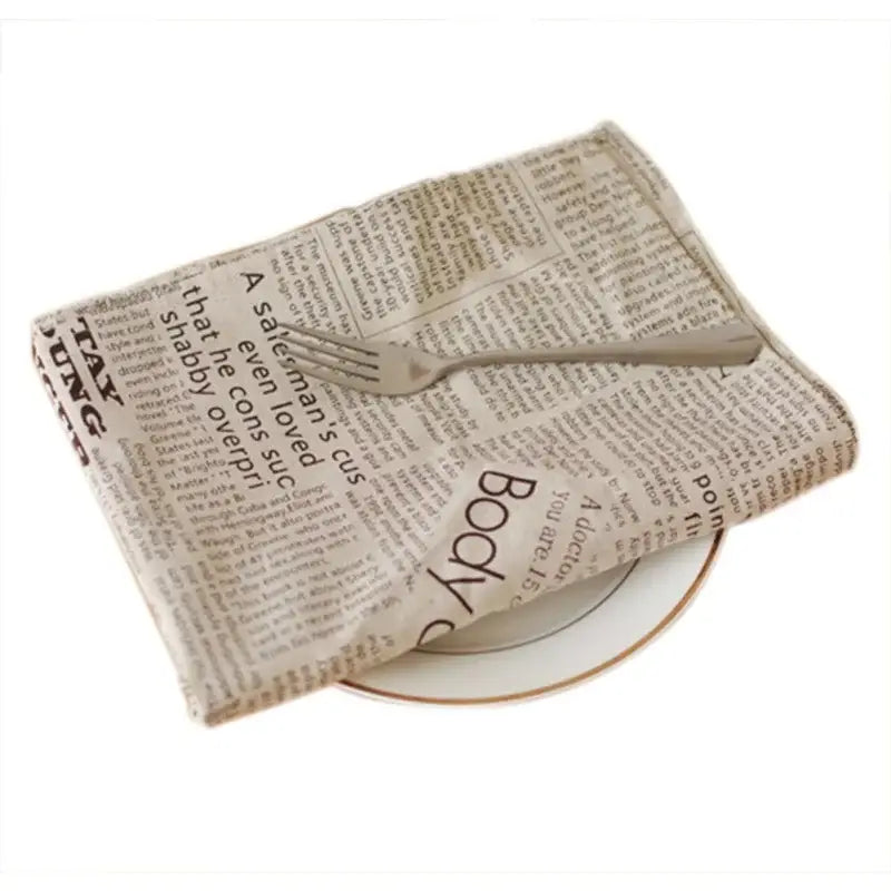 A beige newspaper printed napkin folded over a white plate used as english newspaper style photography props