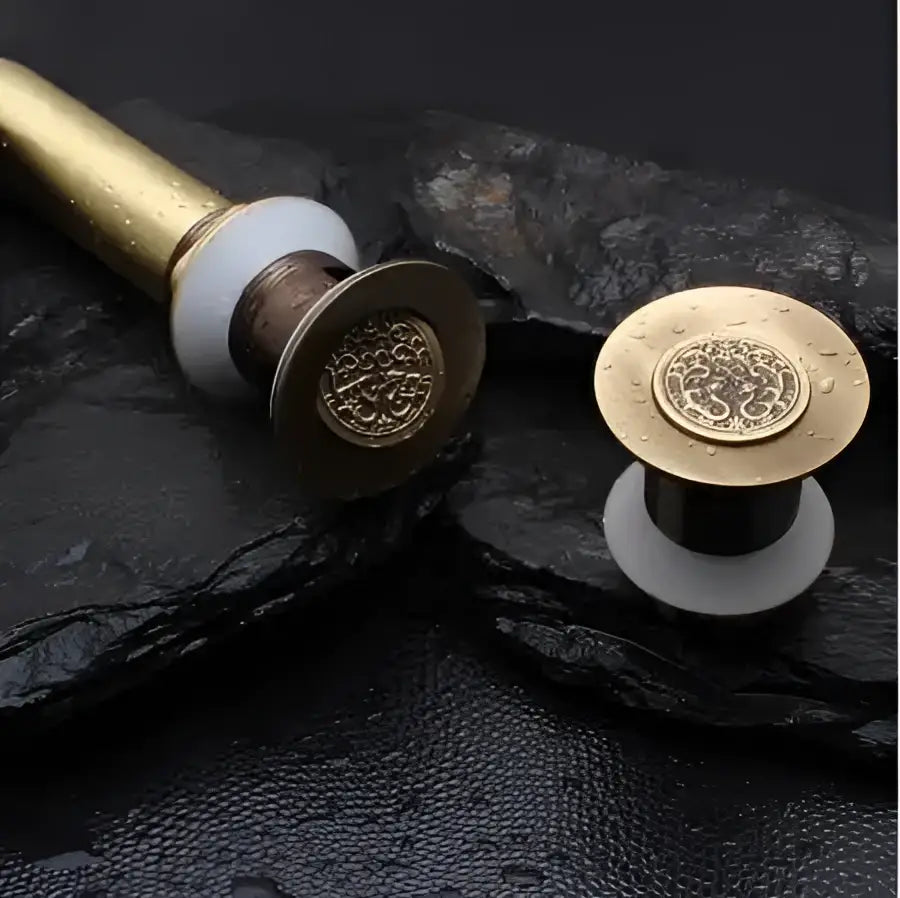 Engraved brass bathroom sink pop up drain stopper with gold-toned tree of life design and white ceramic base decorbites brass bathroom