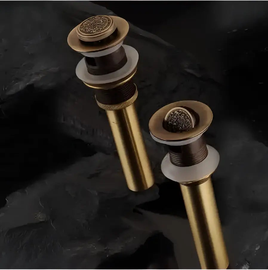 Two elegant engraved brass bathroom sink pop up drain stoppers with ornate circular tops and brushed metallic finish