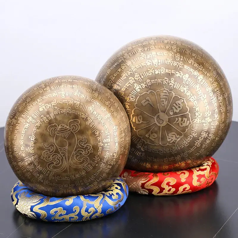 Two bronze-colored engraved tibetan singing bowls with sanskrit script and lotus design for meditation decor