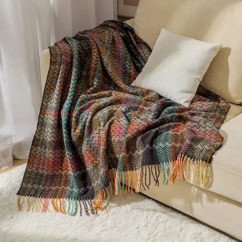 A cozy multicolored ethnic wave woven tassel throw blanket with fringed edges draped over a beige sofa