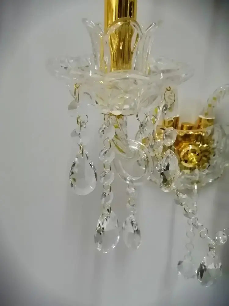 A european gold crystal wall lamp with clear teardrop crystals and gold-toned metal accents for bedroom use