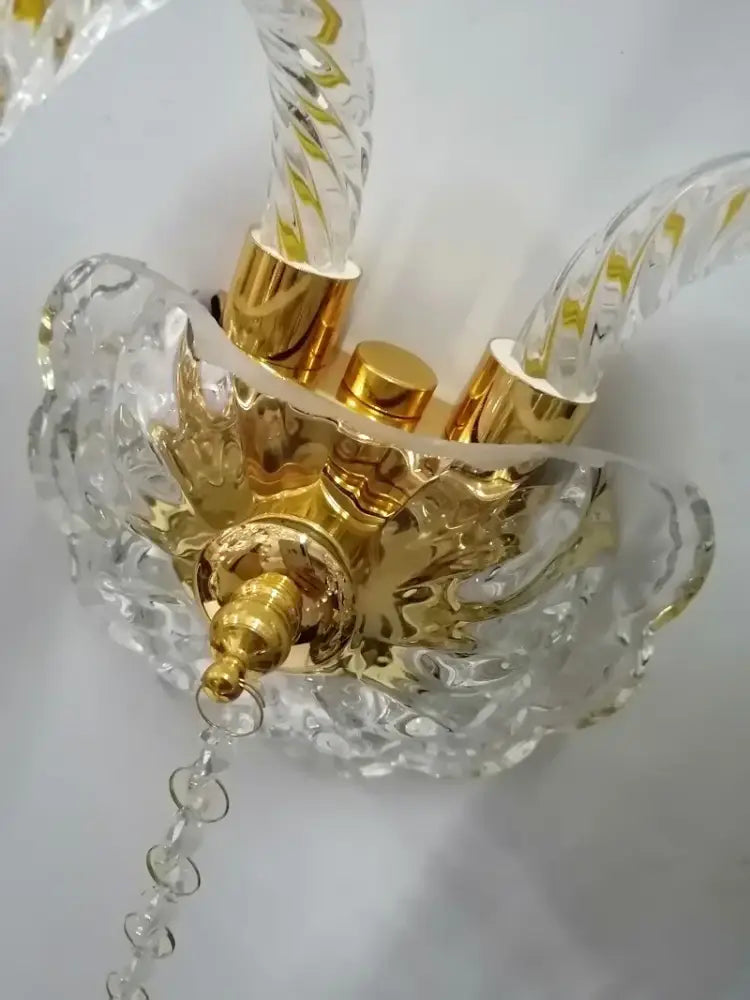 A clear twisted glass crystal wall lamp with gold-toned metal accents and a decorative crystal base for bedroom use