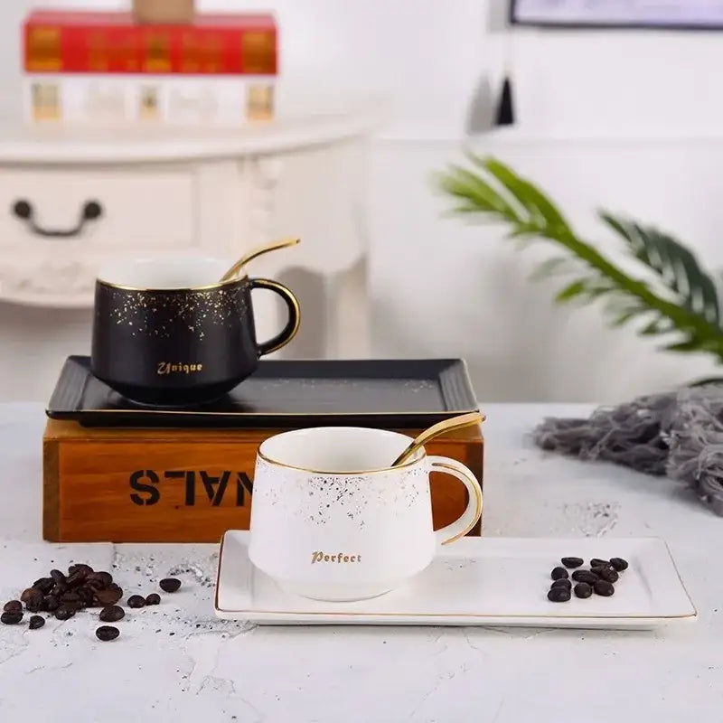 White ceramic coffee cup set with gold rim and speckled finish featuring a matching spoon on a rectangular tray