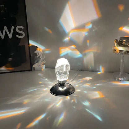 Faceted crystal diamond table lamp with clear prism and black metallic base casting colorful rainbow light patterns