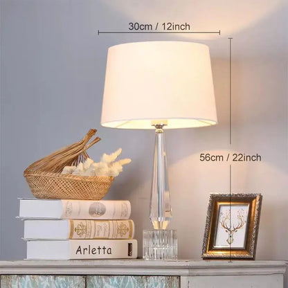 Faceted decorbites crystal table lamp with clear crystal base and off-white fabric shade for bedroom lighting