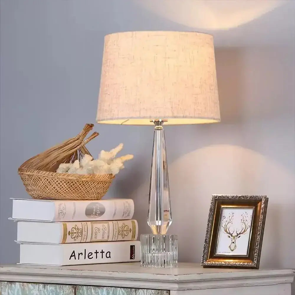 Faceted crystal table lamp with remote control featuring a clear crystal base and beige linen shade for bedroom use