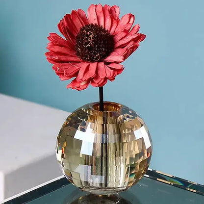 A faceted gold crystal ball aroma diffuser with a geometric base holding a vibrant red dried flower for bedroom decor
