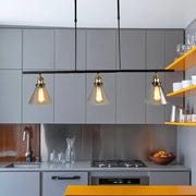 Three clear glass farmhouse cone shade pendant lights with brass fixtures hang above kitchen counter in black finish