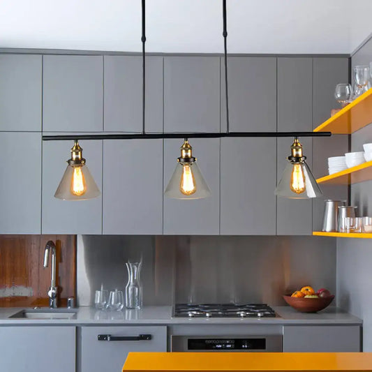 Three clear glass farmhouse cone shade pendant lights with brass fixtures hang above kitchen counter in black finish