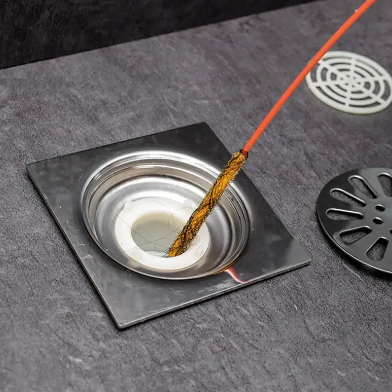 Orange incense stick with charred tip resting in a stainless steel drain for decorbites drain cleaner brush use