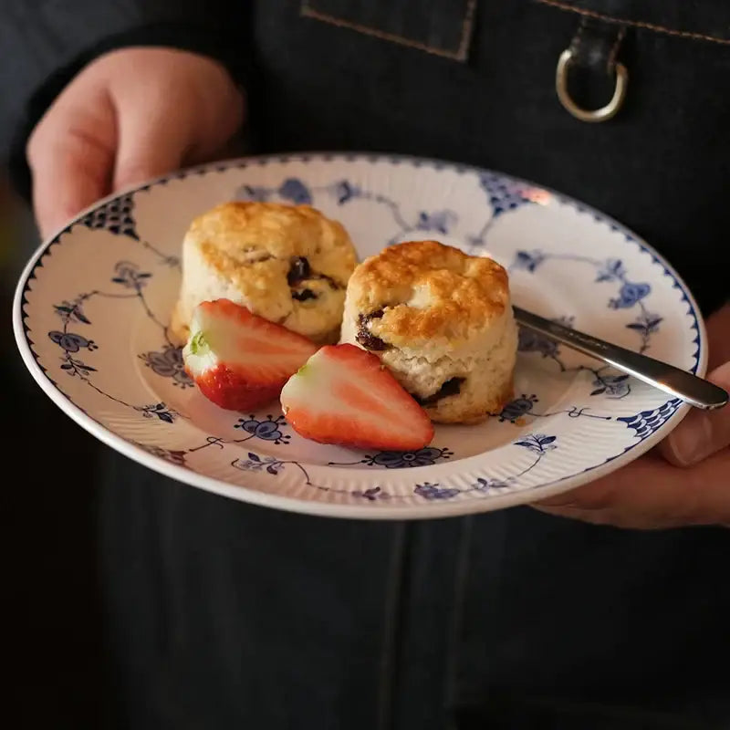 A white and blue floral ceramic dinner plate with scalloped edge holding scones and sliced strawberries for decorbites ceramic dinner