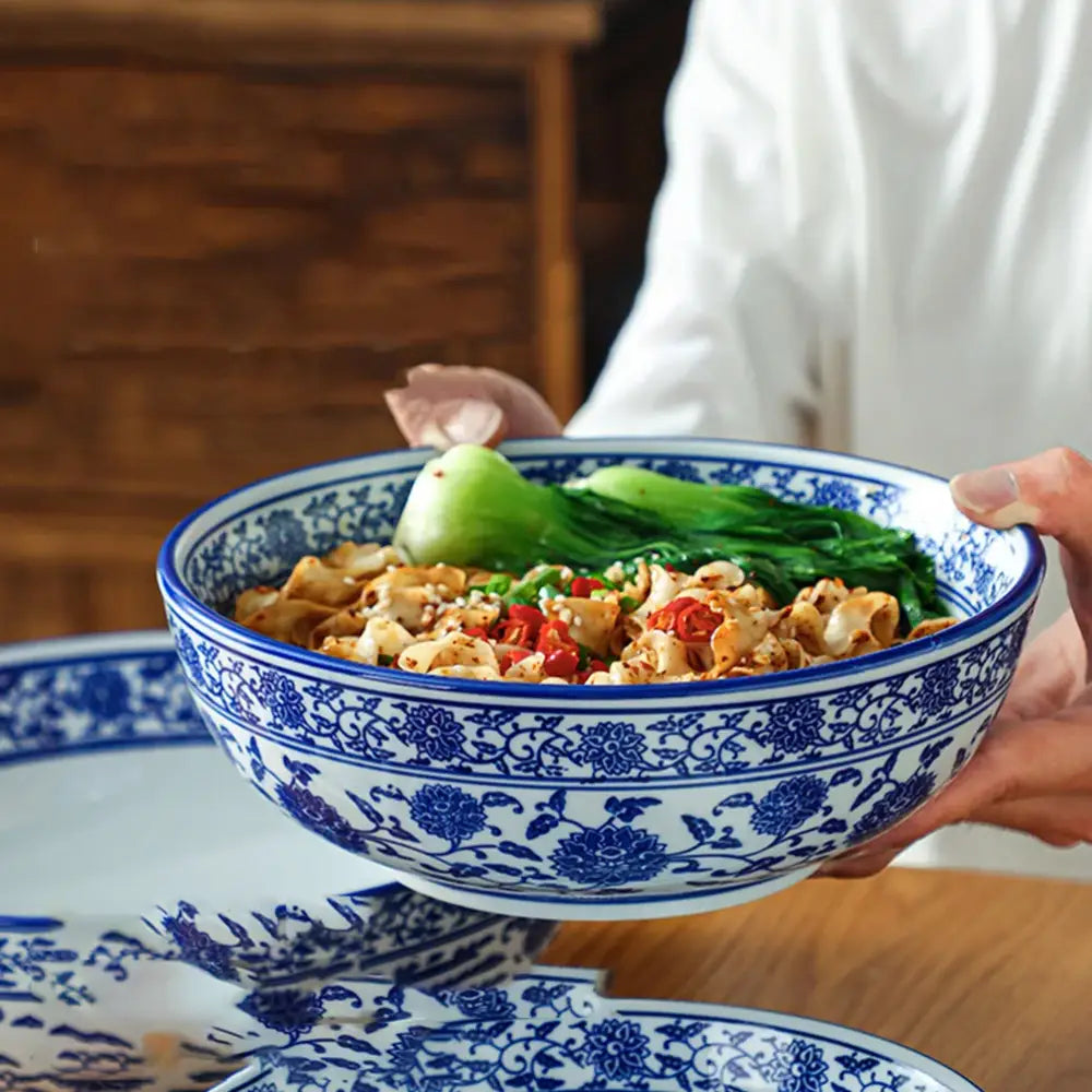 A blue and white ceramic soup bowl with intricate floral patterns filled with colorful noodles by decorbites blue