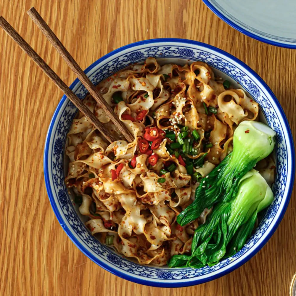 Floral blue and white ceramic soup bowl with wide noodles topped with chili flakes and bok choy by decorbites blue
