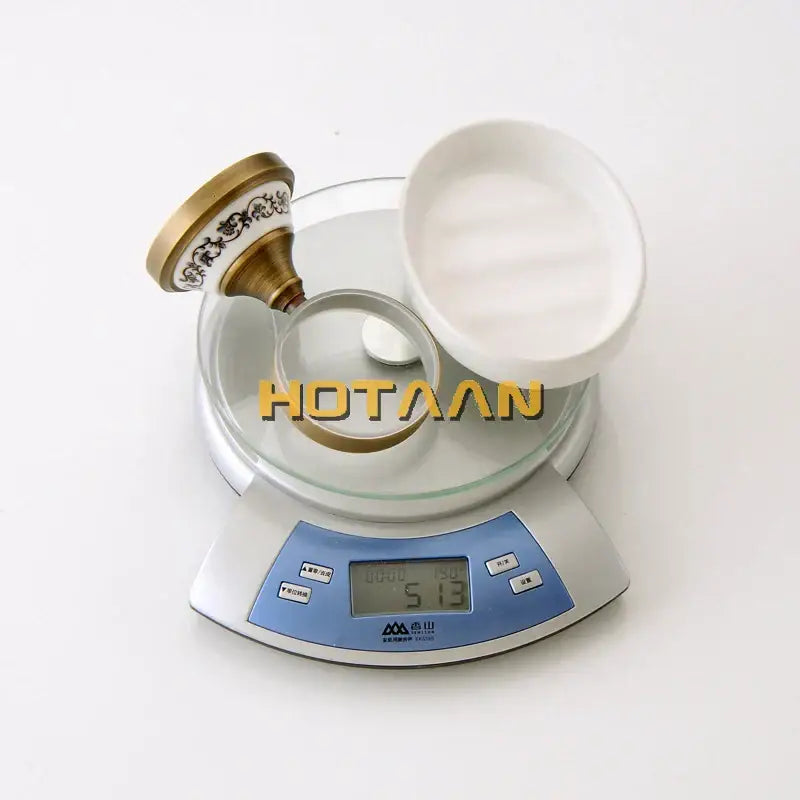 White ceramic dish with decorbites brass soap holder and ornate gold-toned faucet handle on digital scale