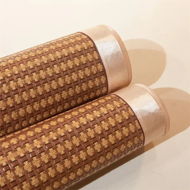 Two rolled floral brown woven cooling rattan mats with shiny beige ribbon edges for bedroom bed pad use