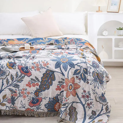 A double cotton bohemian throw blanket in off-white with vibrant blue orange and pink floral patterns and fringed edges