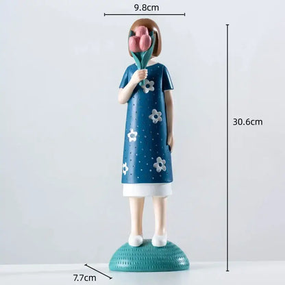 A blue resin figure sculpture of a girl in a floral dress holding pink tulips on a textured teal base for living room decor