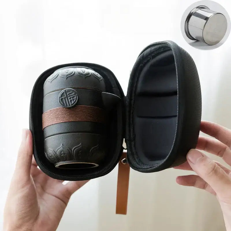 Black pottery tea set with embossed floral patterns and circular chinese emblem secured by brown woven strap travel bag