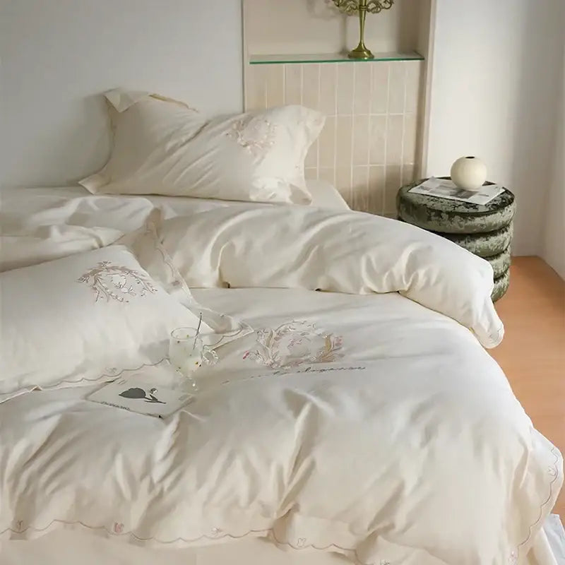 Cream-colored satin duvet cover set with delicate floral embroidery and scalloped edges for elegant bedroom decor