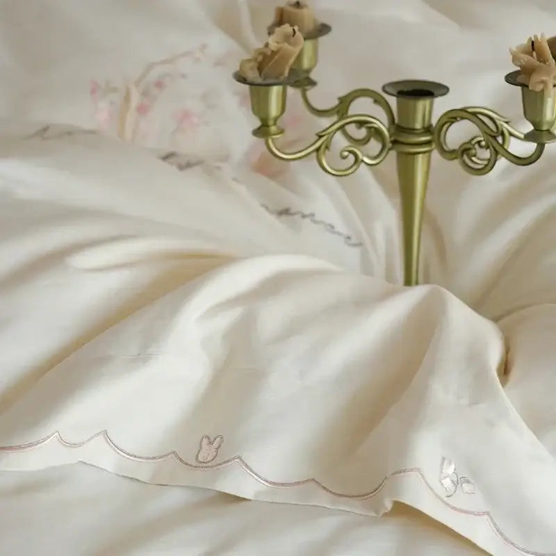 Ivory satin pillowcase with scalloped edges and silver embroidered bunny motifs in floral embroidered cream duvet cover set