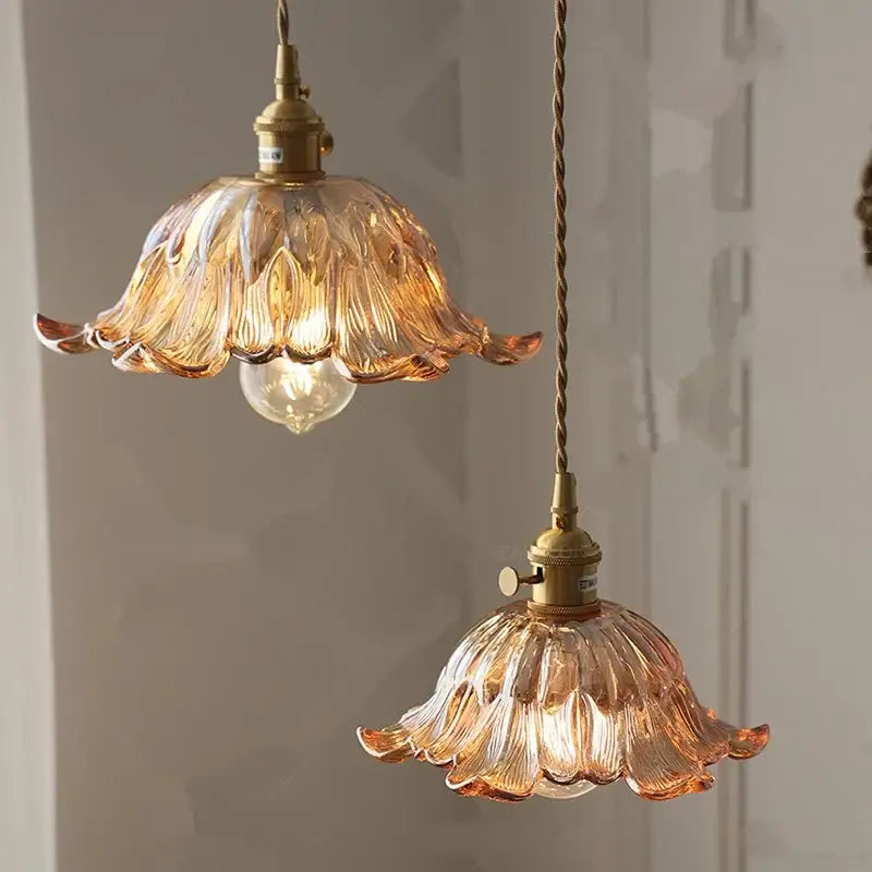 Two amber-colored glass pendant lights with floral petal design and brass fixtures for dining room use