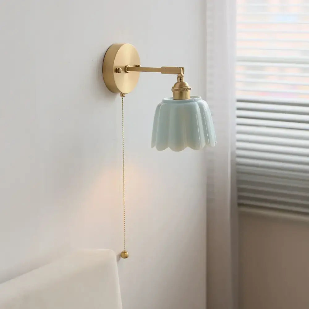A delicate brass wall light fixture with a pale blue fluted glass shade and gold pull chain for bedroom use