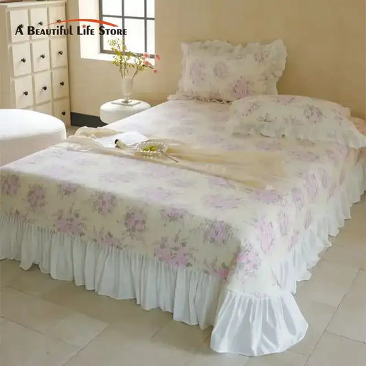 A delicate white quilted bedspread set with soft pink floral patterns and a ruffled hemline for bedroom decor