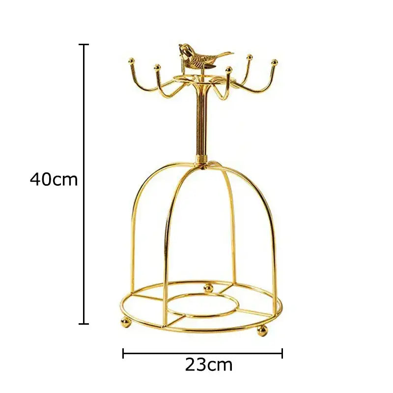 Gold-colored metal birdcage-style jewelry stand with small golden bird atop central pole beside floral pink purple coffee mug set