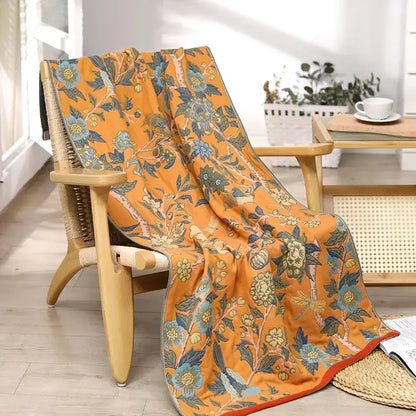 Orange floral-patterned cotton gauze bath towel with blue and green blossoms draped over wooden chair for decorbites cotton gauze bathroom decor
