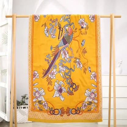A vibrant yellow silk scarf with a colorful bird and floral design complements floral pink and yellow cotton gauze bath towel decor