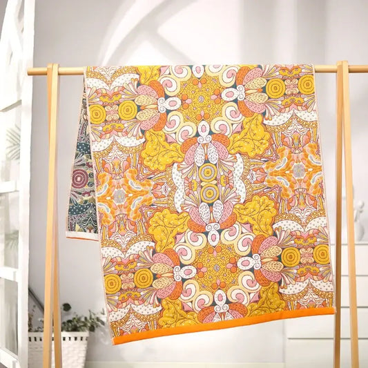 A vibrant yellow and pink floral patterned cotton gauze bath towel with bold orange border hanging on wooden rack decorbites cotton gauze bath