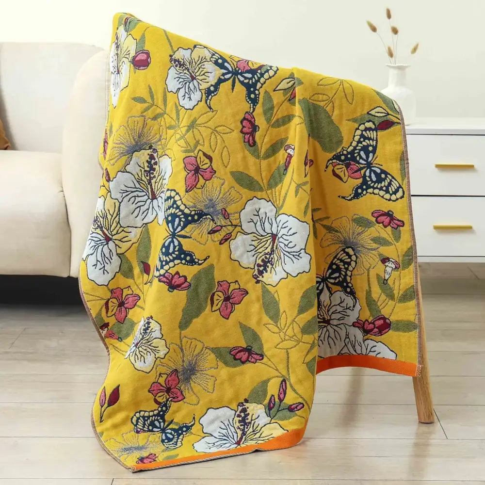 A vibrant yellow cotton gauze bath towel with pink white and blue butterfly floral pattern for bathroom decor