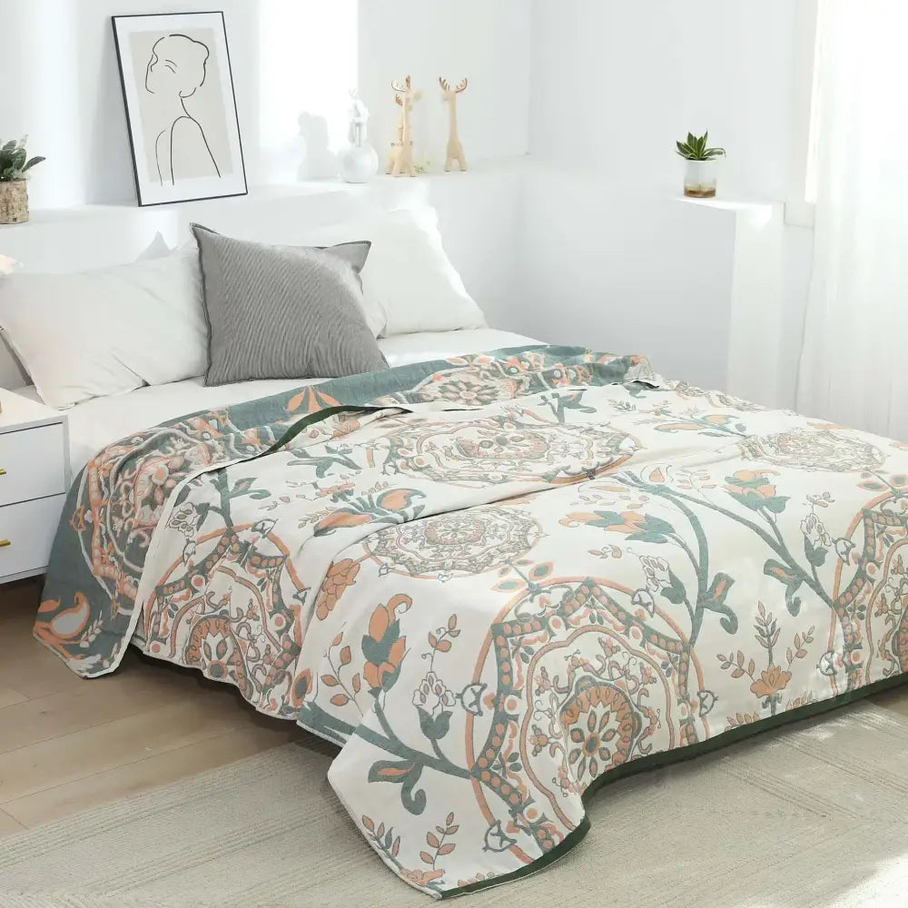 A cream cotton gauze summer blanket with intricate floral and paisley pattern in muted orange green and brown tones