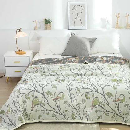 A soft light green and gray patterned cotton gauze summer blanket with birds on branches, ideal as a bedroom throw