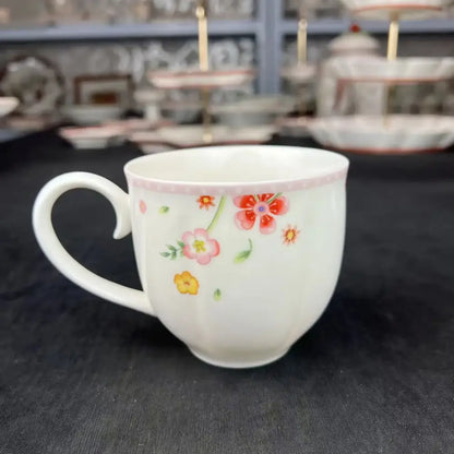 A white ceramic mug with delicate pink and yellow floral patterns and a pink rim from a tulip dinnerware set