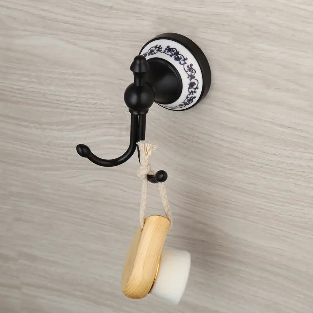 Black stainless steel bathroom towel hook with decorative white and blue porcelain base holding wooden bath brush