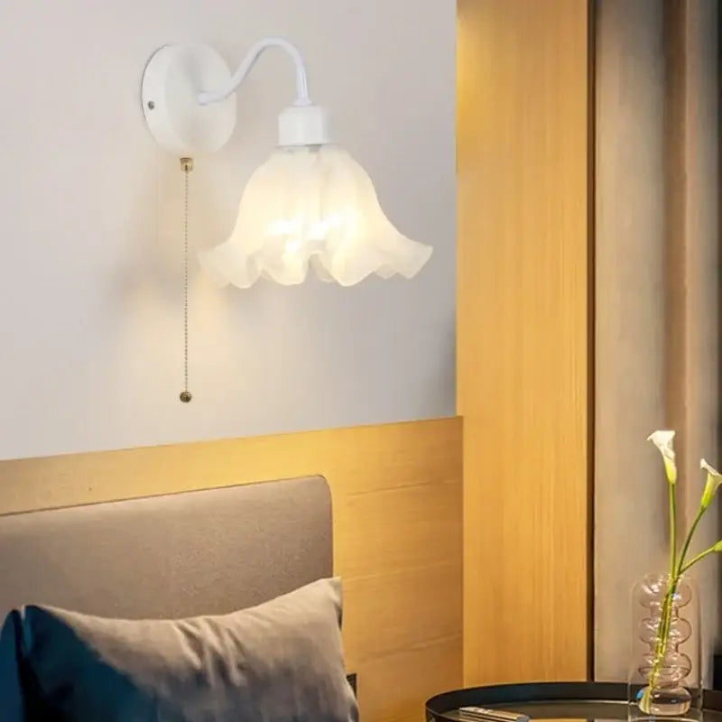 Floral white glass wall sconce with delicate ruffled shade, curved arm, and pull chain switch for stair light