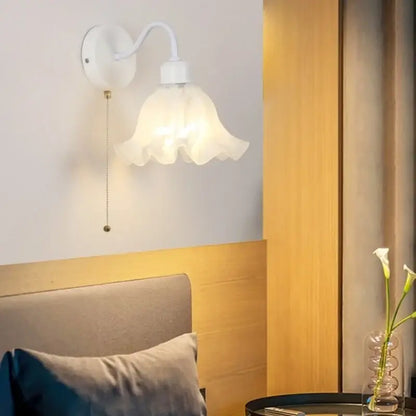 Floral white glass wall sconce with delicate ruffled shade, curved arm, and pull chain switch for stair light