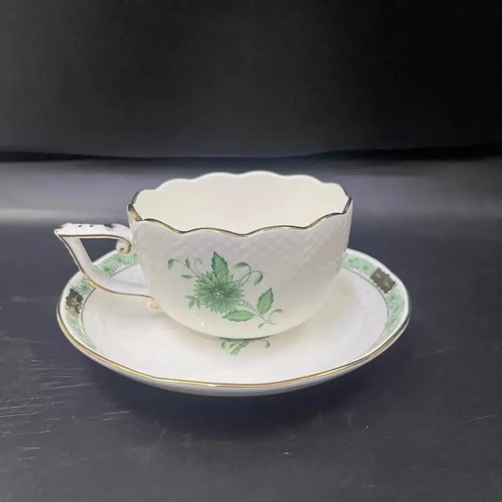 A delicate white porcelain tea cup with gold trim and green floral design in a floral white and green cup set