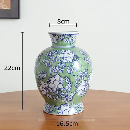 Green ceramic vase with white porcelain floral patterns featuring rounded body and narrow neck for living room decor