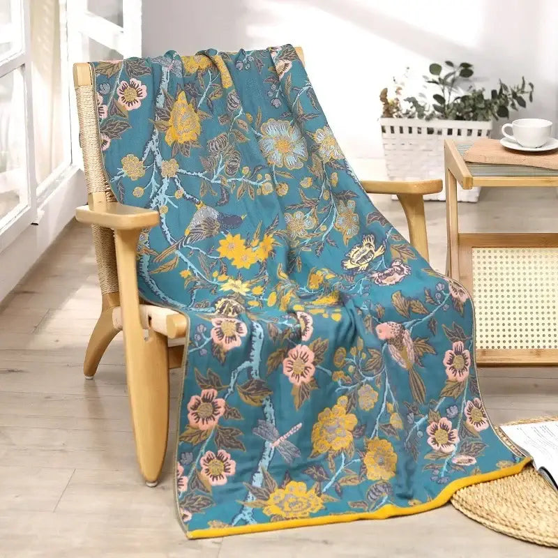 Teal cotton gauze floral bath towel with yellow and pink blossoms, birds, and dragonflies on wooden chair draped fabric