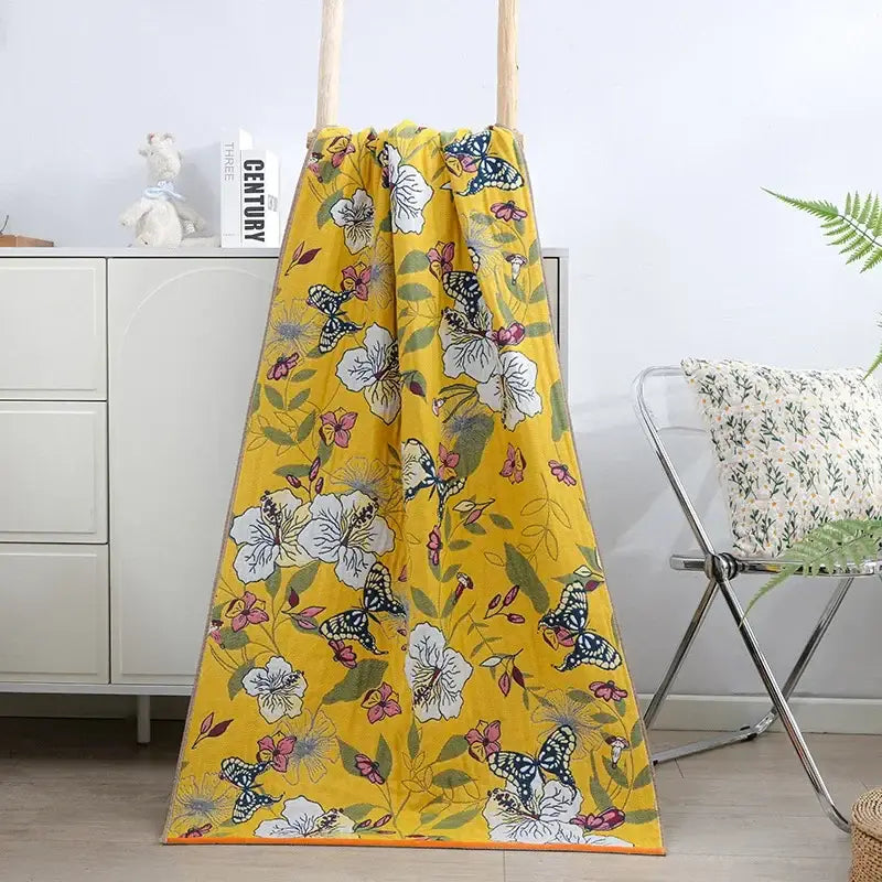 A vibrant yellow bath towel with cotton gauze floral pattern of white flowers pink blossoms and black-and-white butterflies