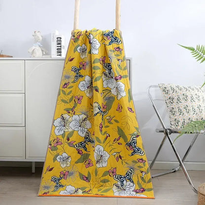 A vibrant yellow bath towel with cotton gauze floral pattern of white flowers pink blossoms and black-and-white butterflies