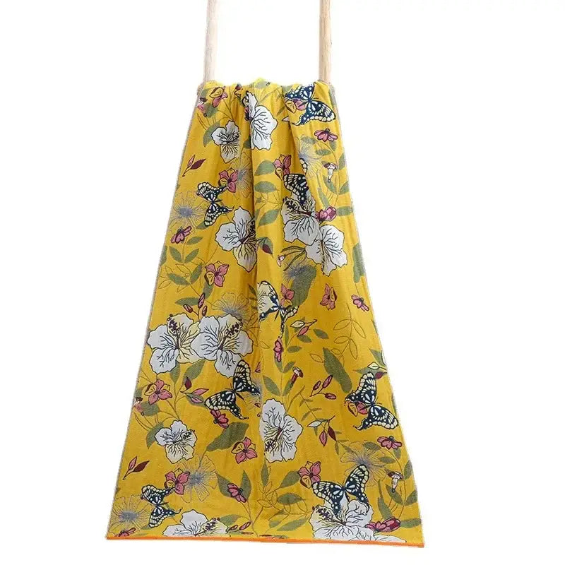 A vibrant yellow cotton gauze floral drawstring bag with white flowers, pink blossoms, and butterflies for decorbites bath towel wrap