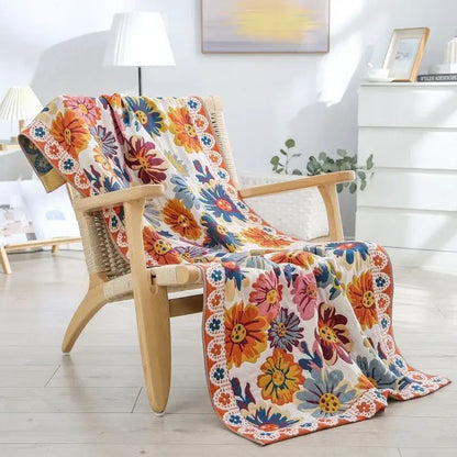 A floral yellow cotton gauze bath towel with bold orange pink and blue blossoms draped on a wooden armchair